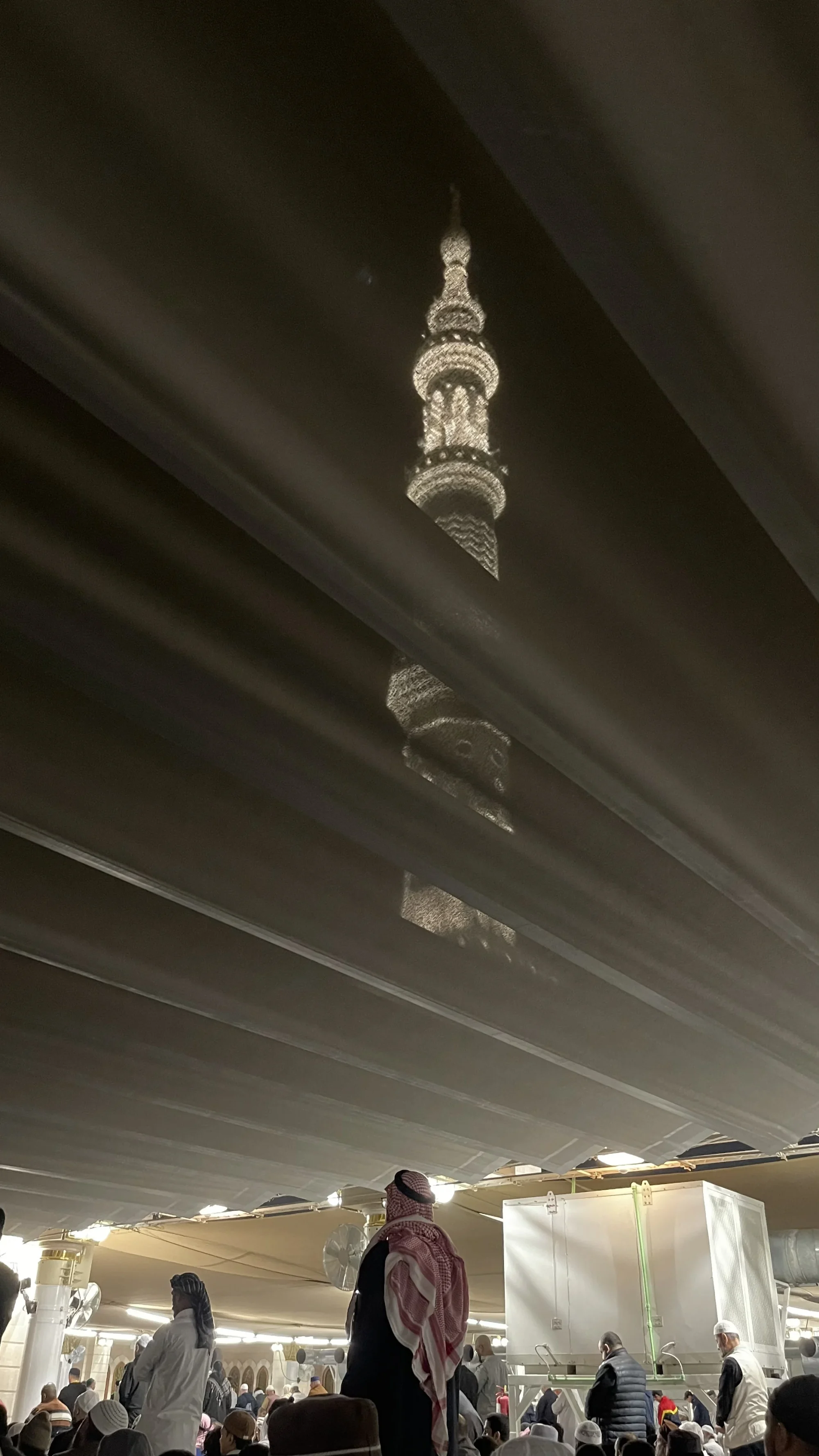 Light from a minaret falling across a dark canopy above a crowd