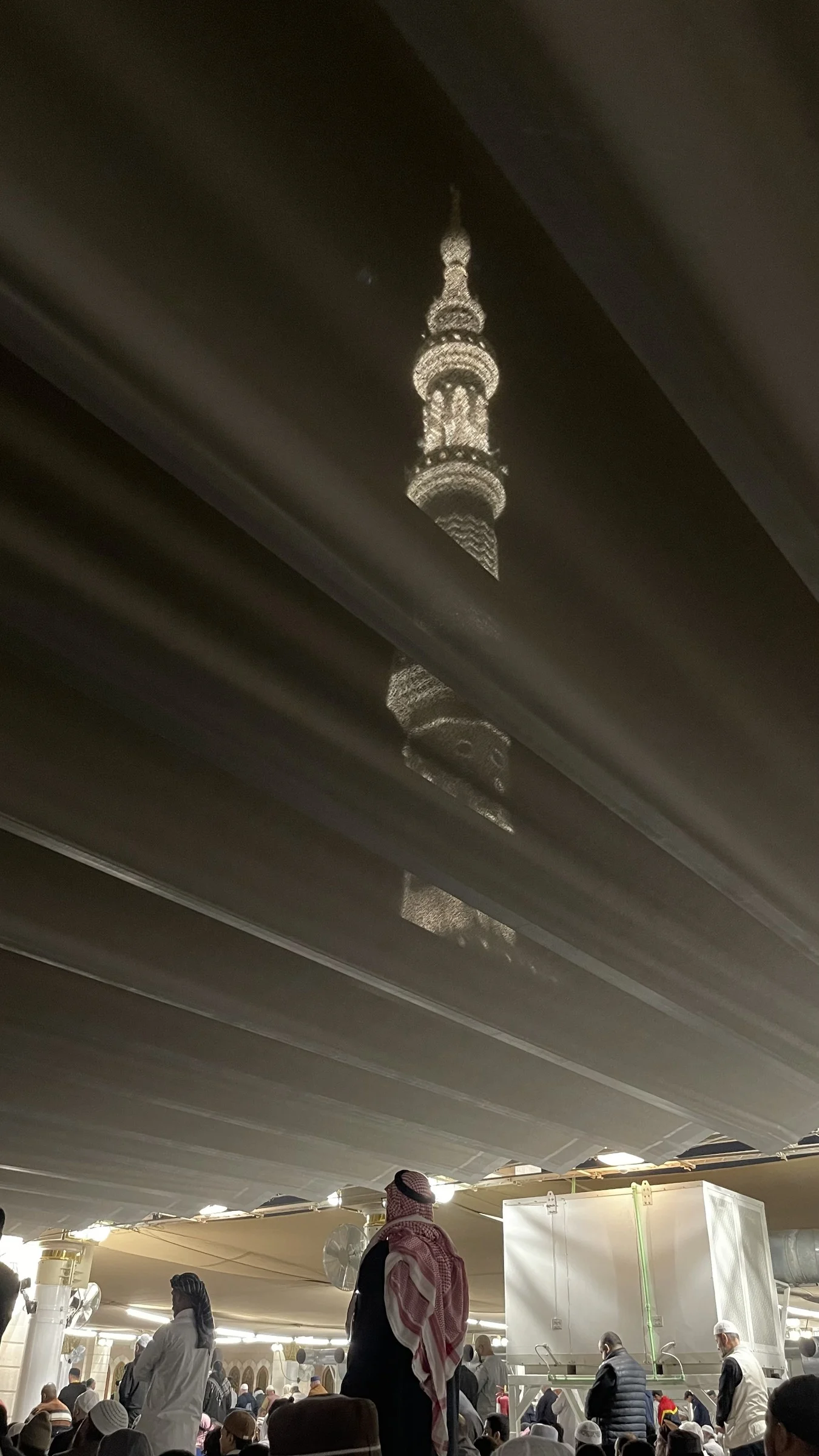 A lit minaret seen through the gap in a great canopy