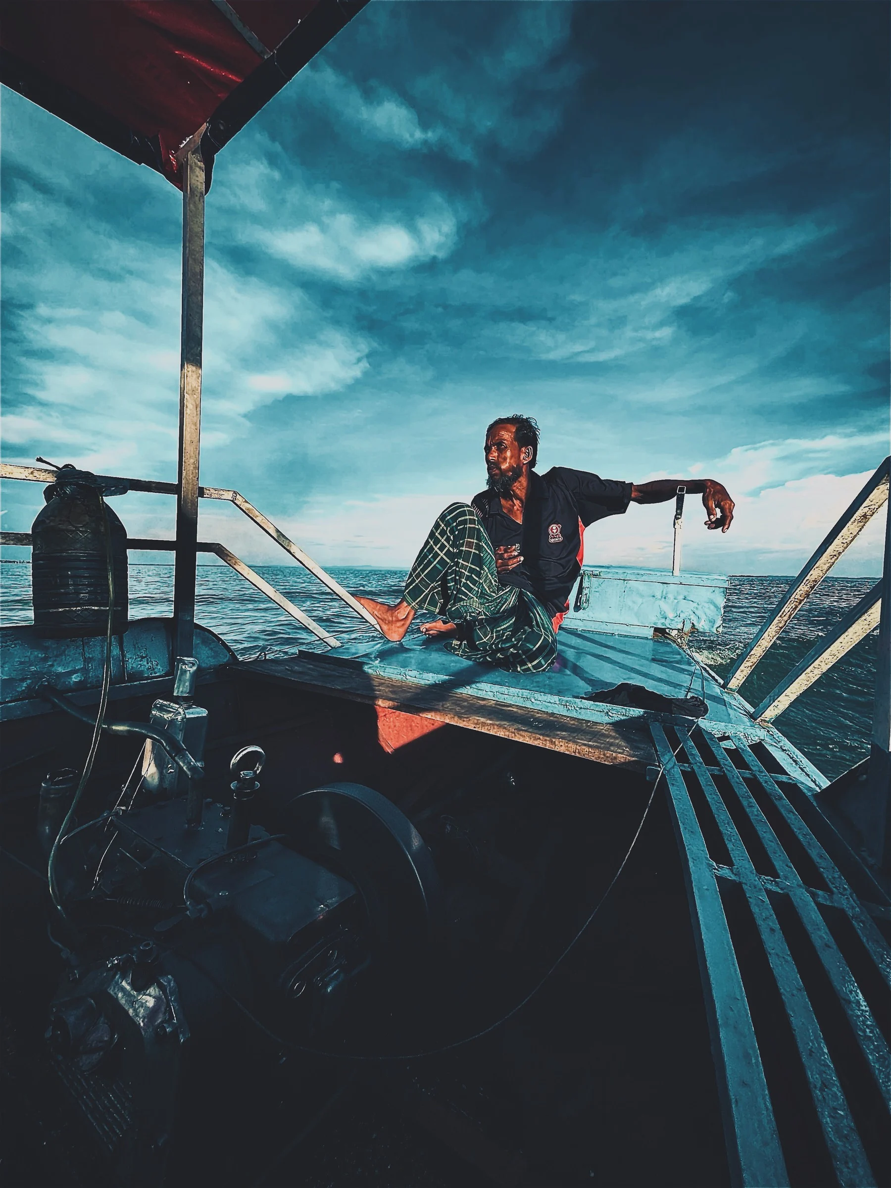 A man sitting on the roof of a boat at sea, one arm on the rail