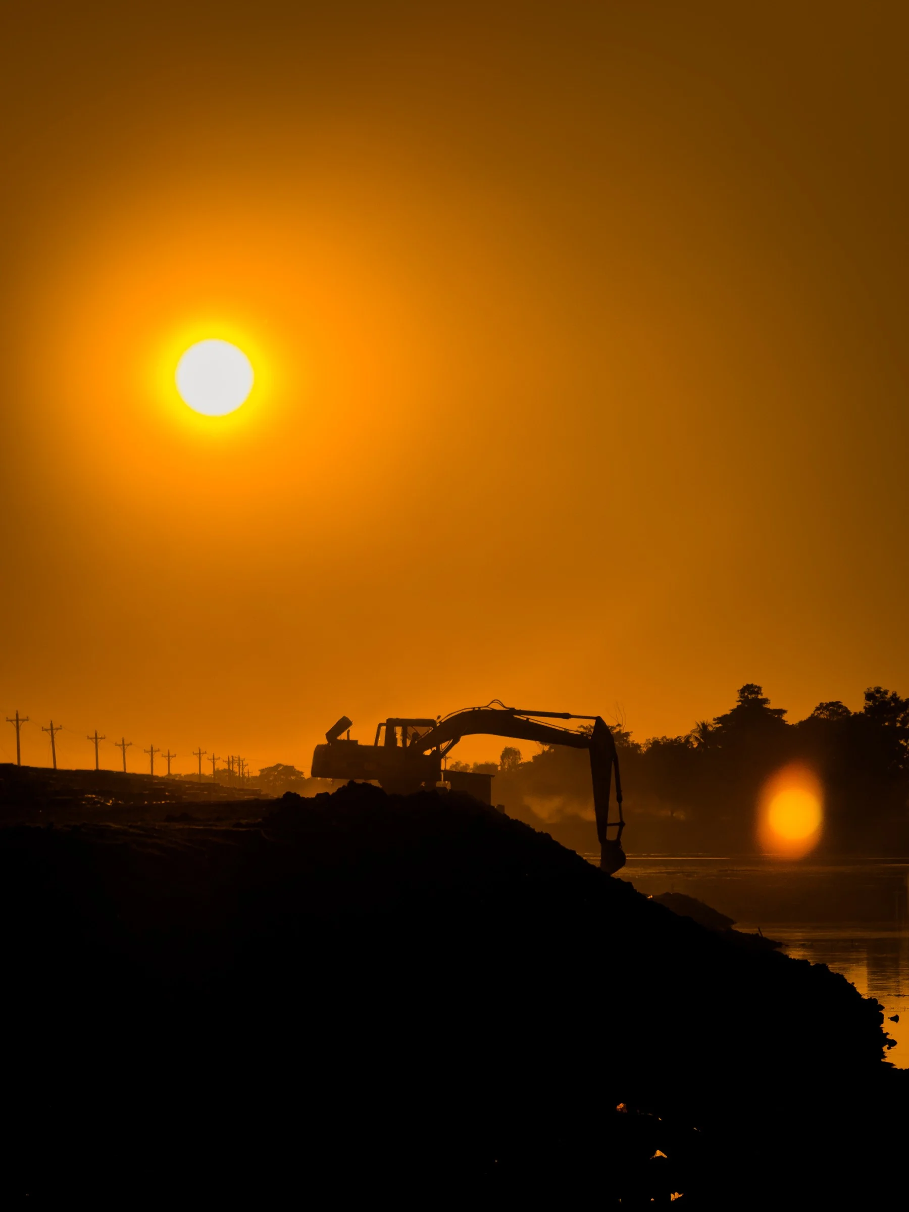 An excavator in silhouette on a bank against a burning sky