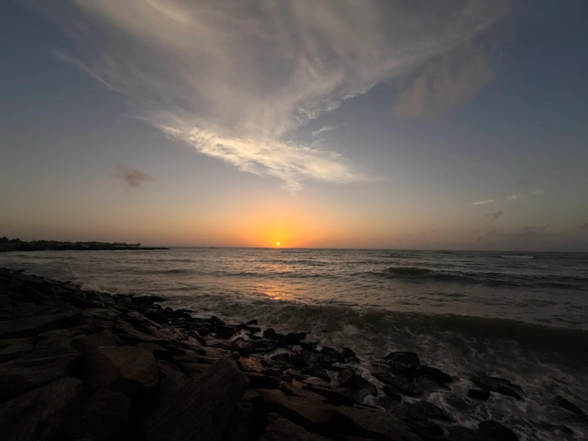 The sun setting over the sea beyond a rocky breakwater