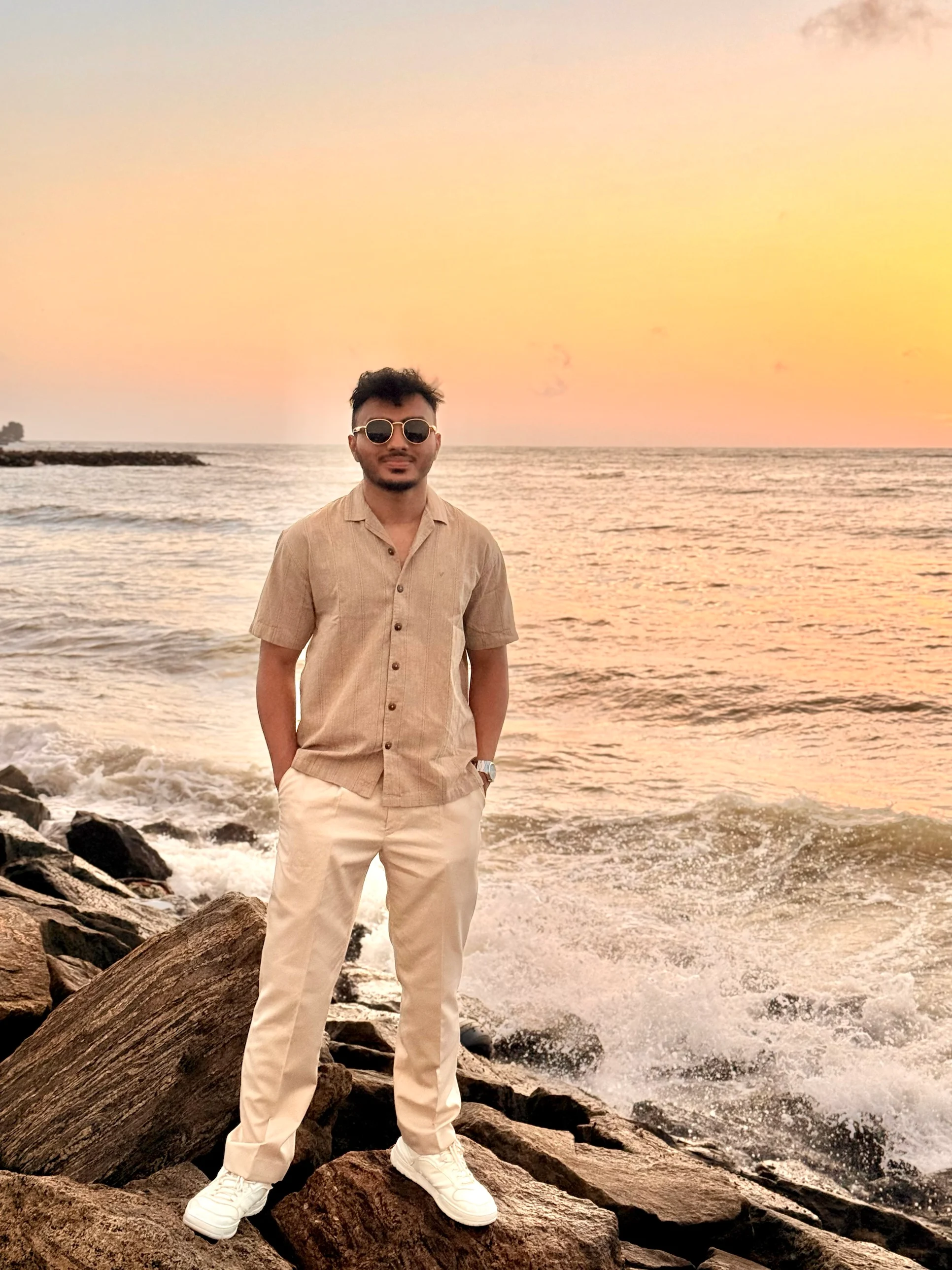 A man standing on rocks at the water's edge at sunset