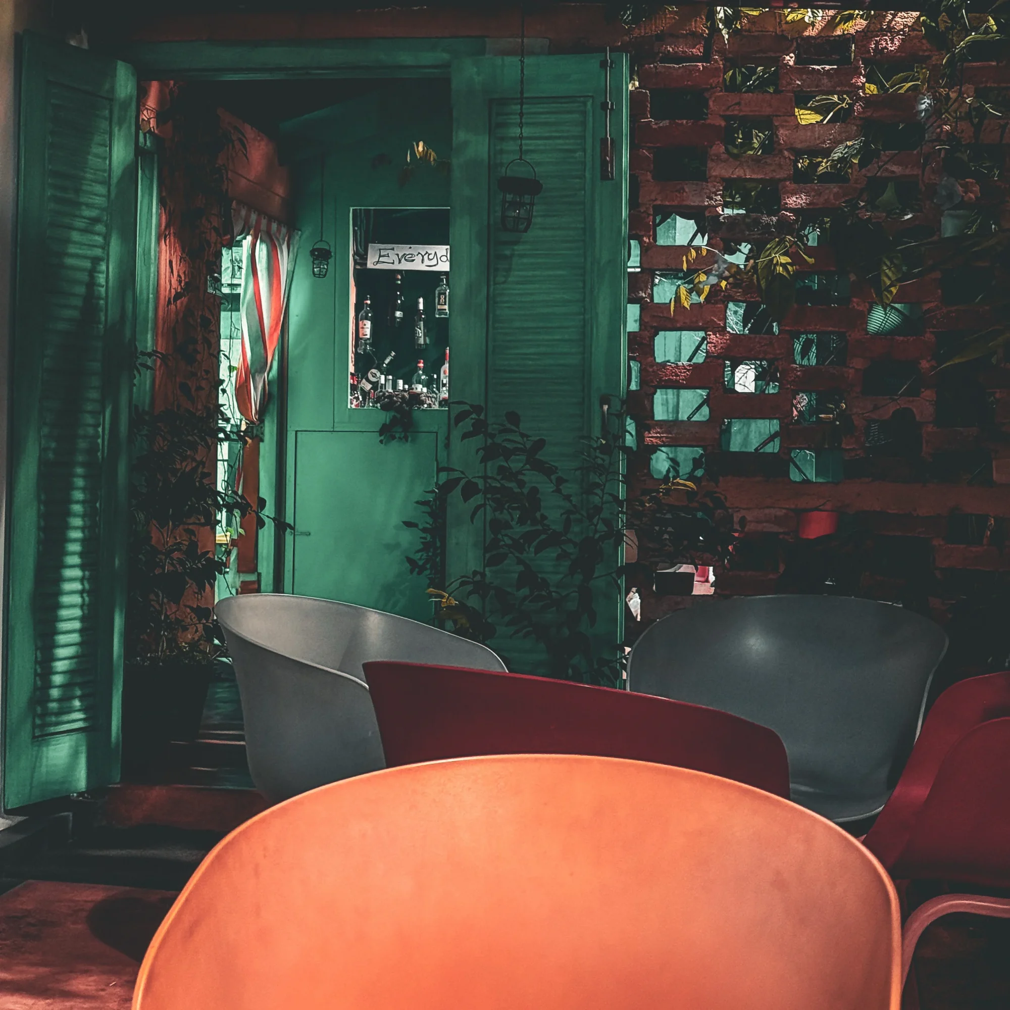 A cafe courtyard with green shutters, a perforated brick wall and coloured chairs