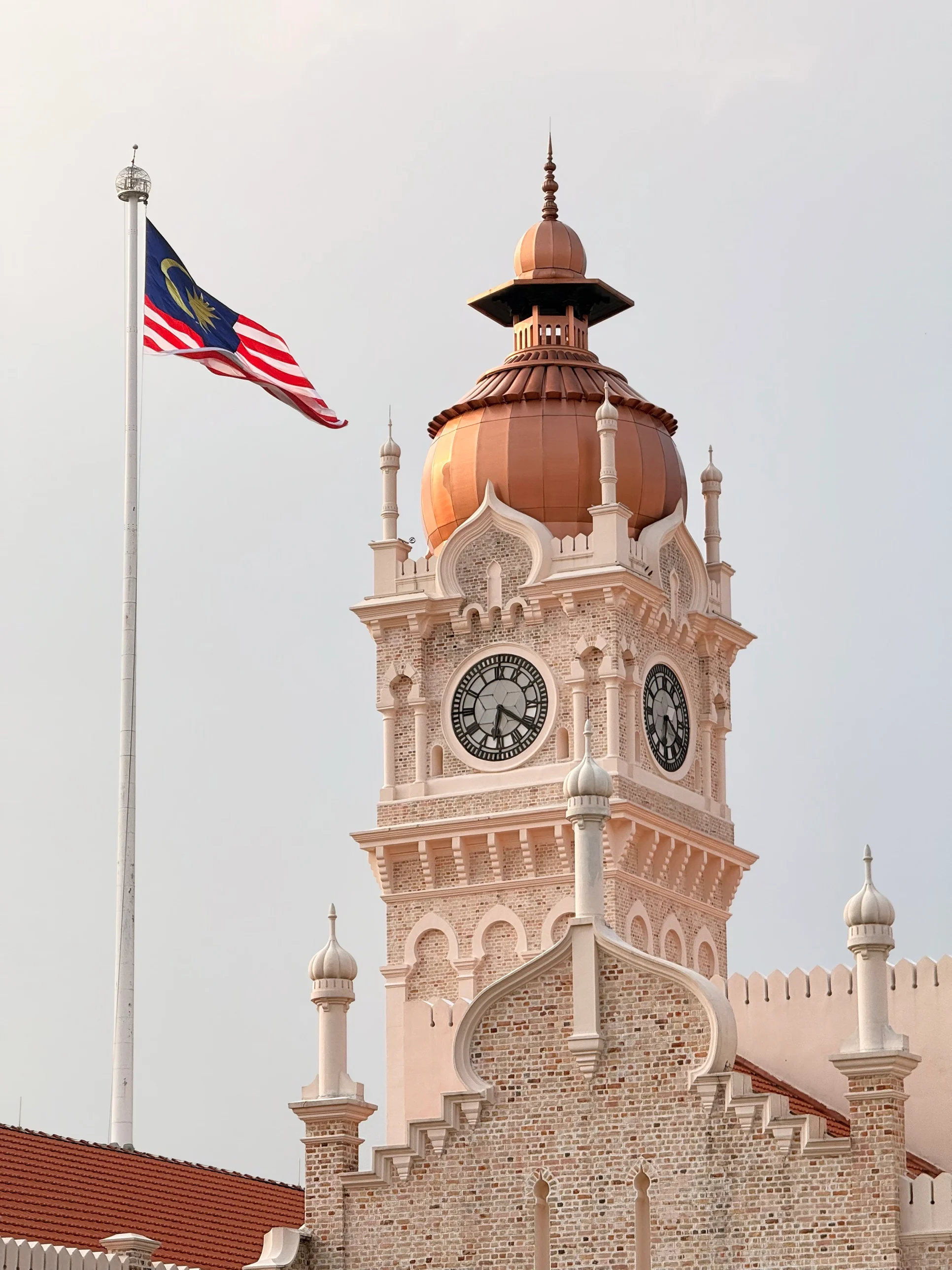 The copper dome and clock face of the Sultan Abdul Samad Building beside a Malaysian flag