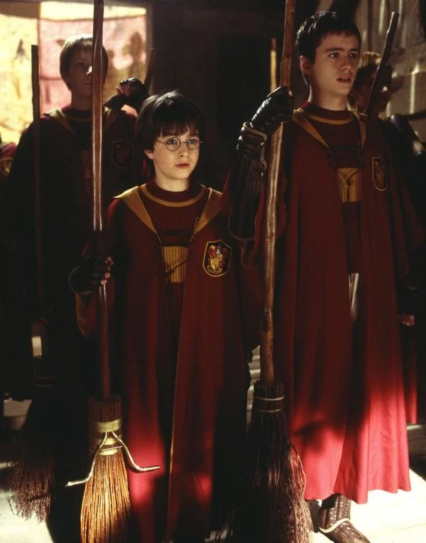 Harry in scarlet Quidditch robes holding a broomstick
