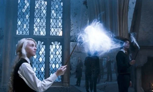 Luna and Harry casting a bright patronus indoors