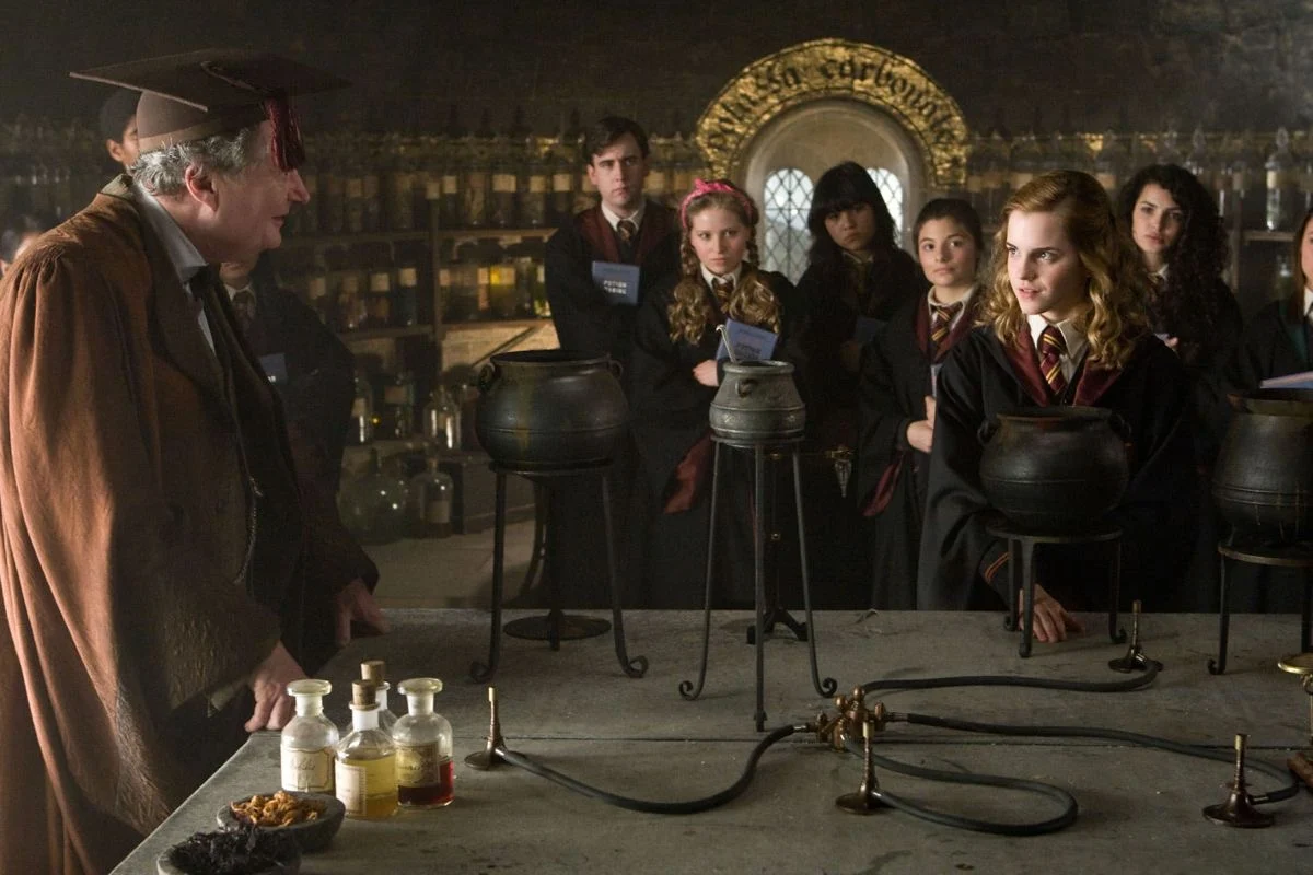 Slughorn addressing a potions class around three cauldrons
