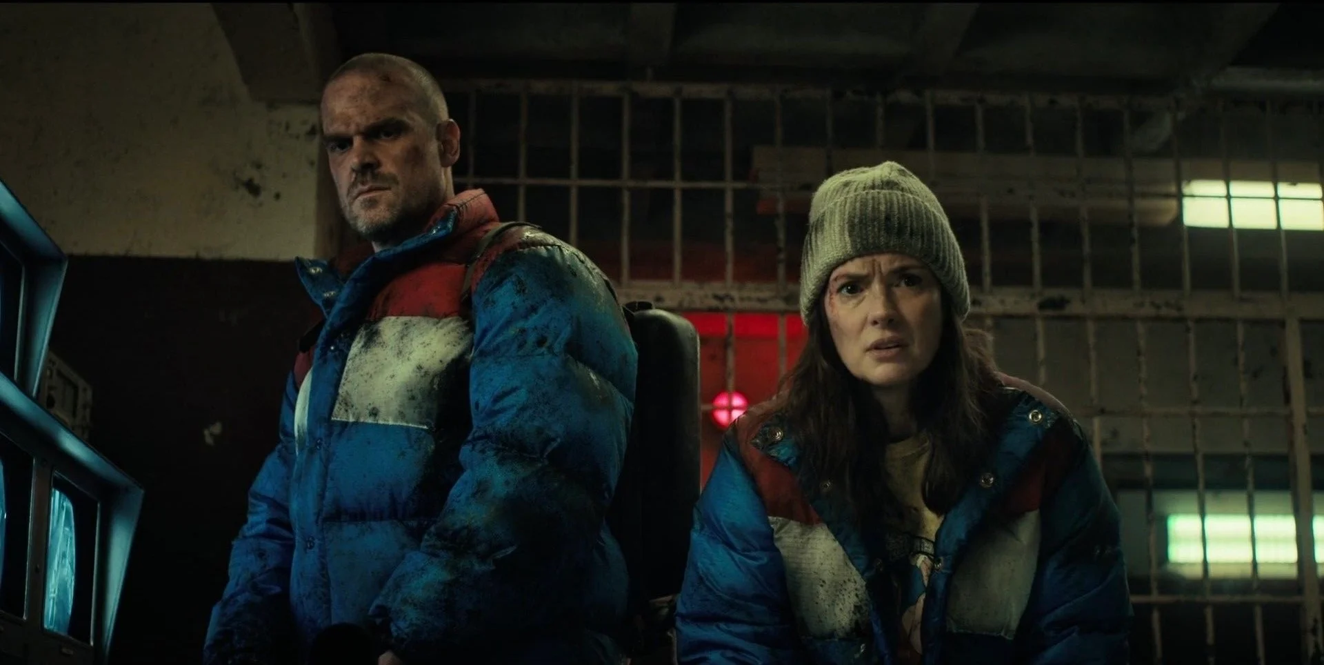 Hopper and Joyce in heavy winter coats inside a dark facility