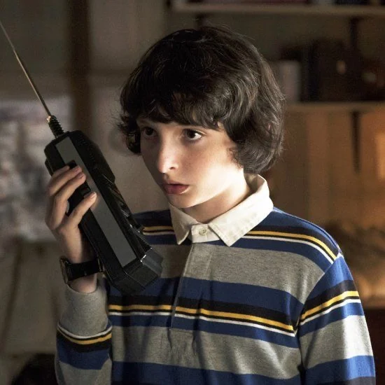 Mike Wheeler holding a walkie talkie to his ear