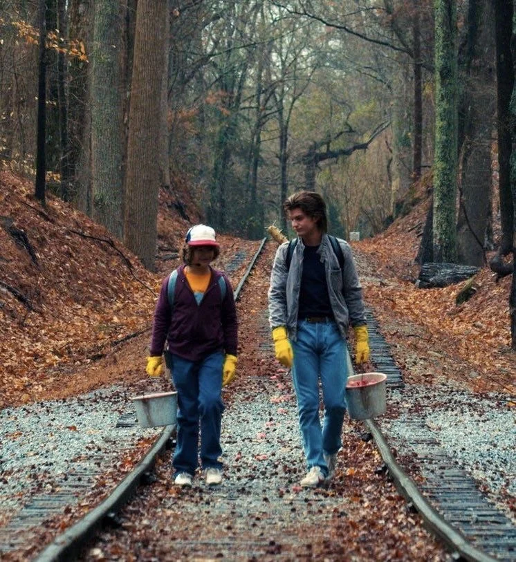 Steve and Dustin walking down railway tracks carrying buckets