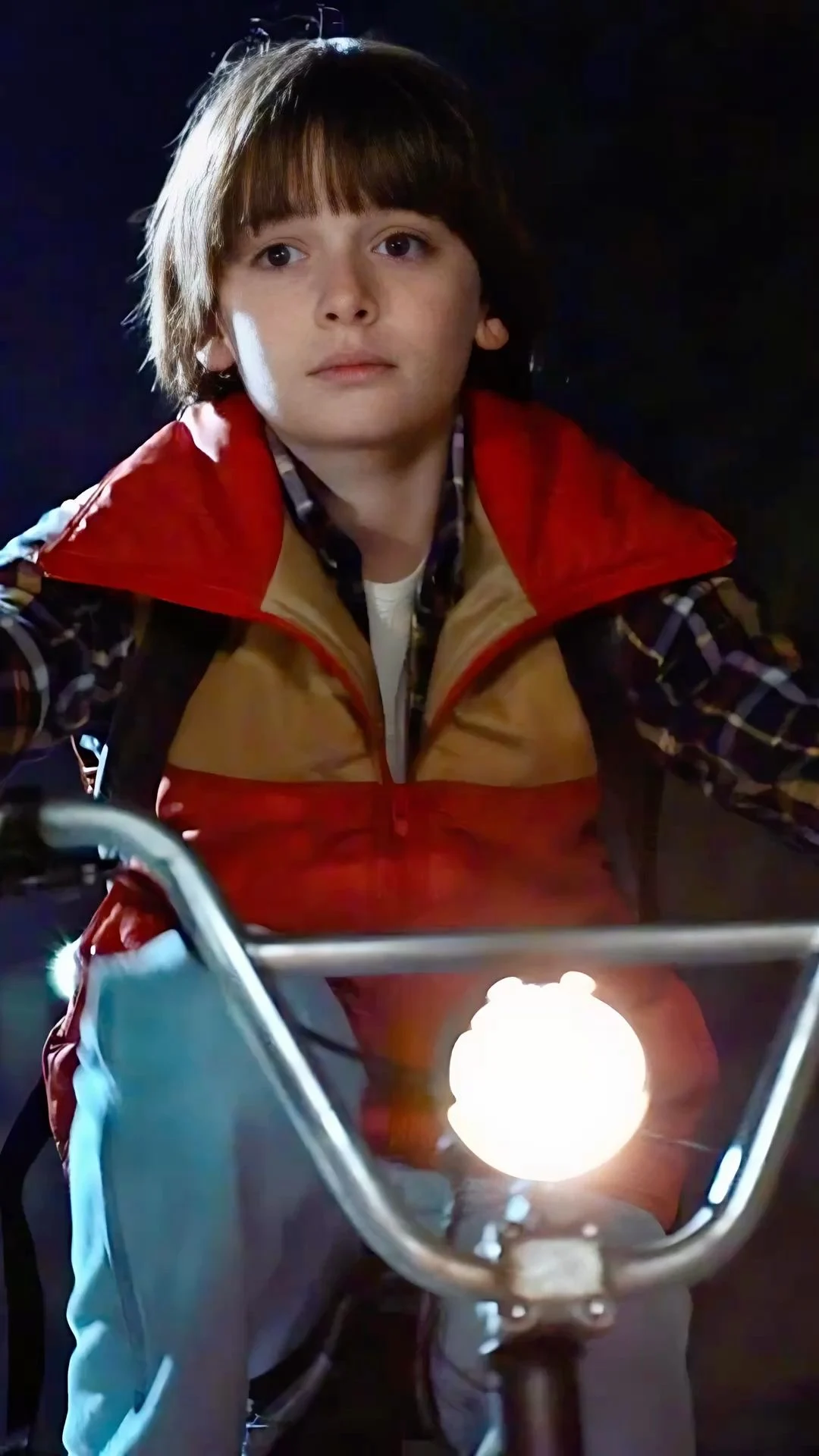 Will Byers on a bicycle at night, headlamp burning